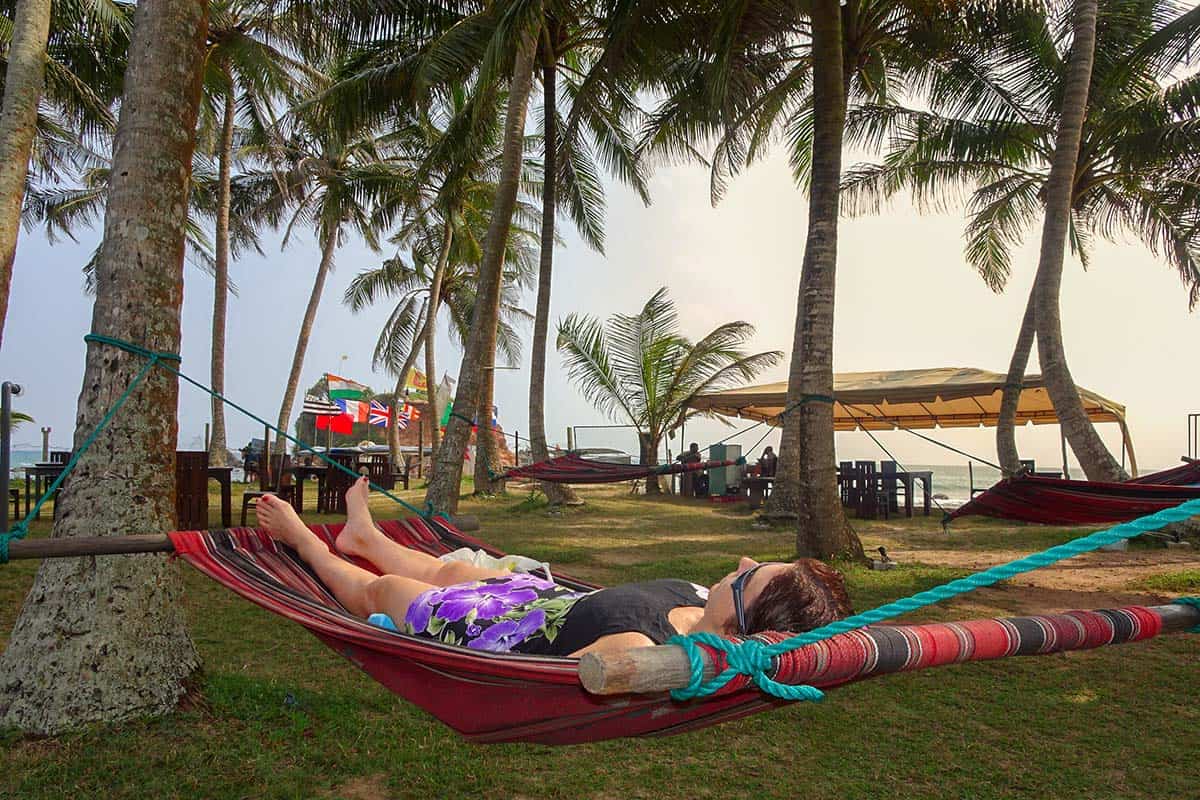 A lady lying in a hammock under palm trees next to a beach