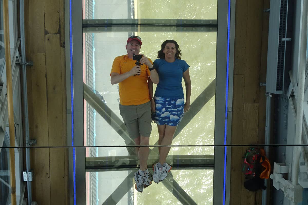 A couple lying on a glass walkway above a river.