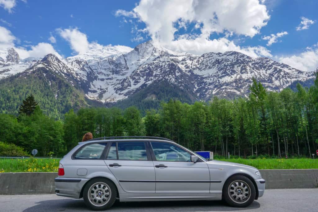 Silver car in forefront of a snowy mountain and pine forest