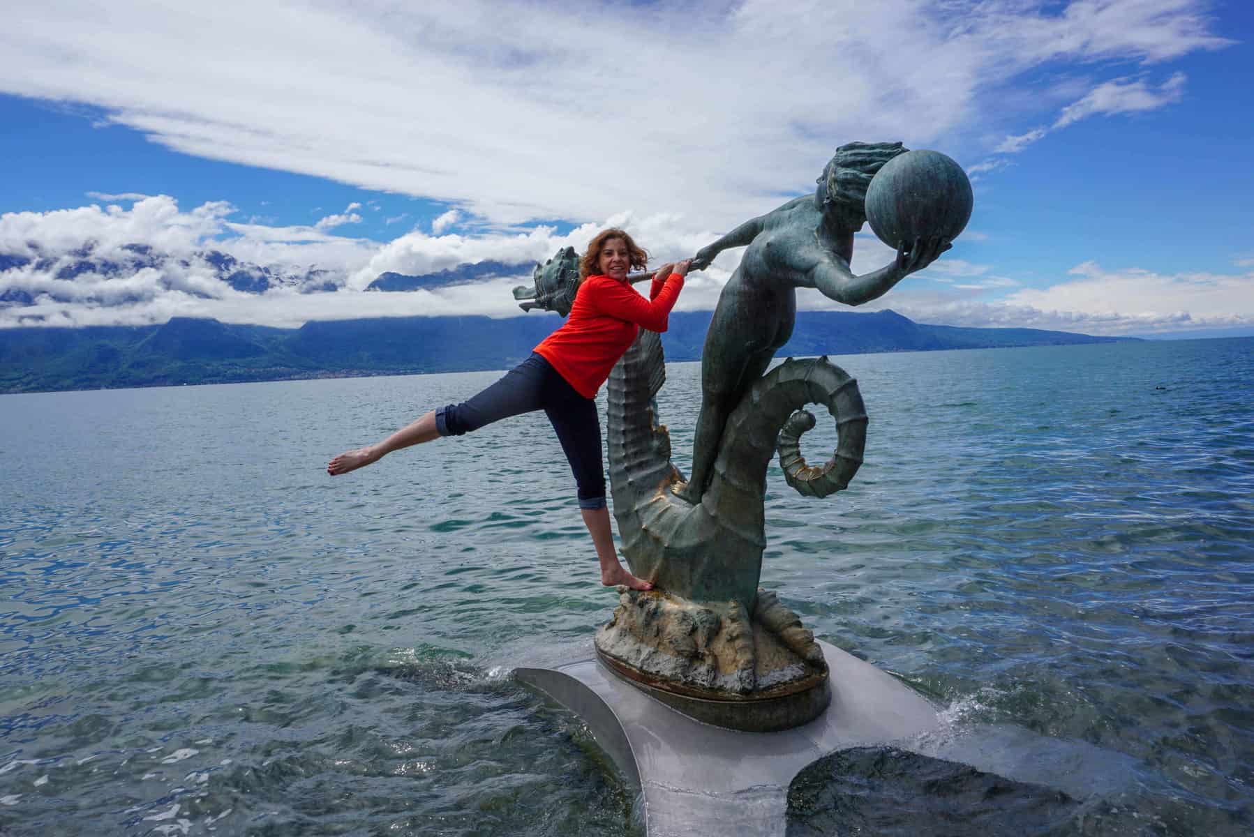 W woman in jeans and red top hanging off a sculpture on a lake