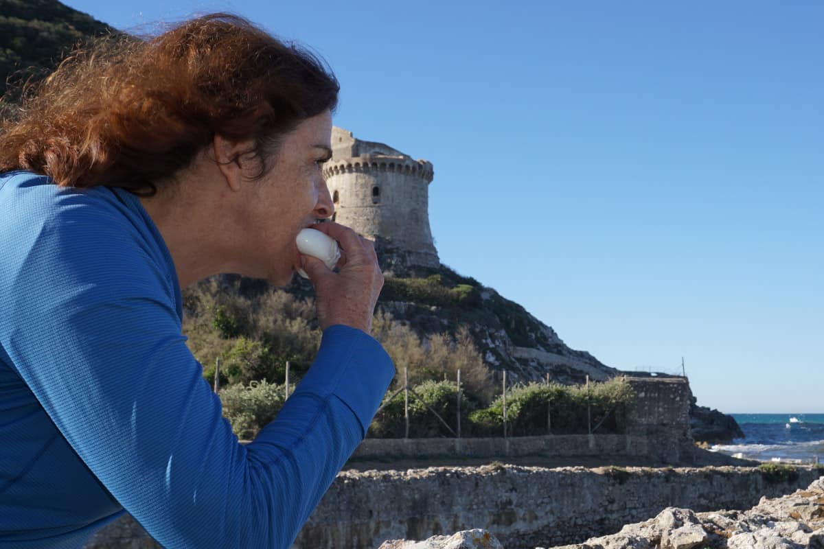 A lady eating cheese next to an ancient tower