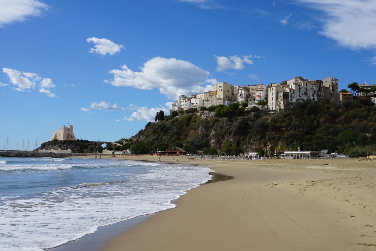 A sandy beach leading to a town on a hill