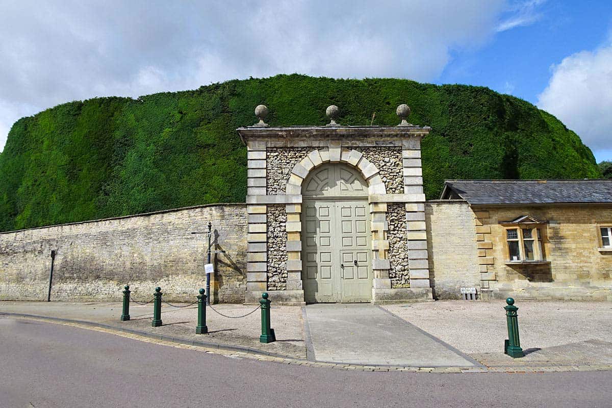 A large gate in a stone fence with a huge hedge