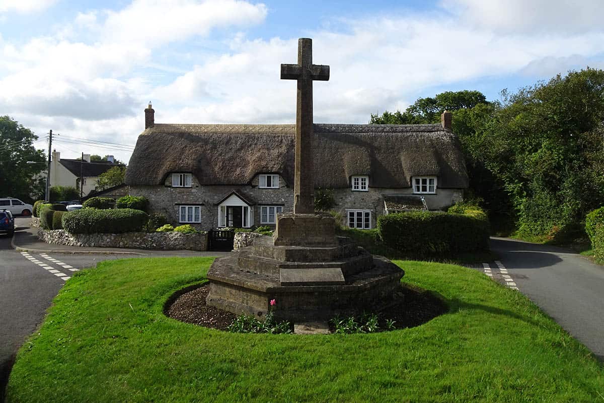 A stone cross in front of as thatched cottage
