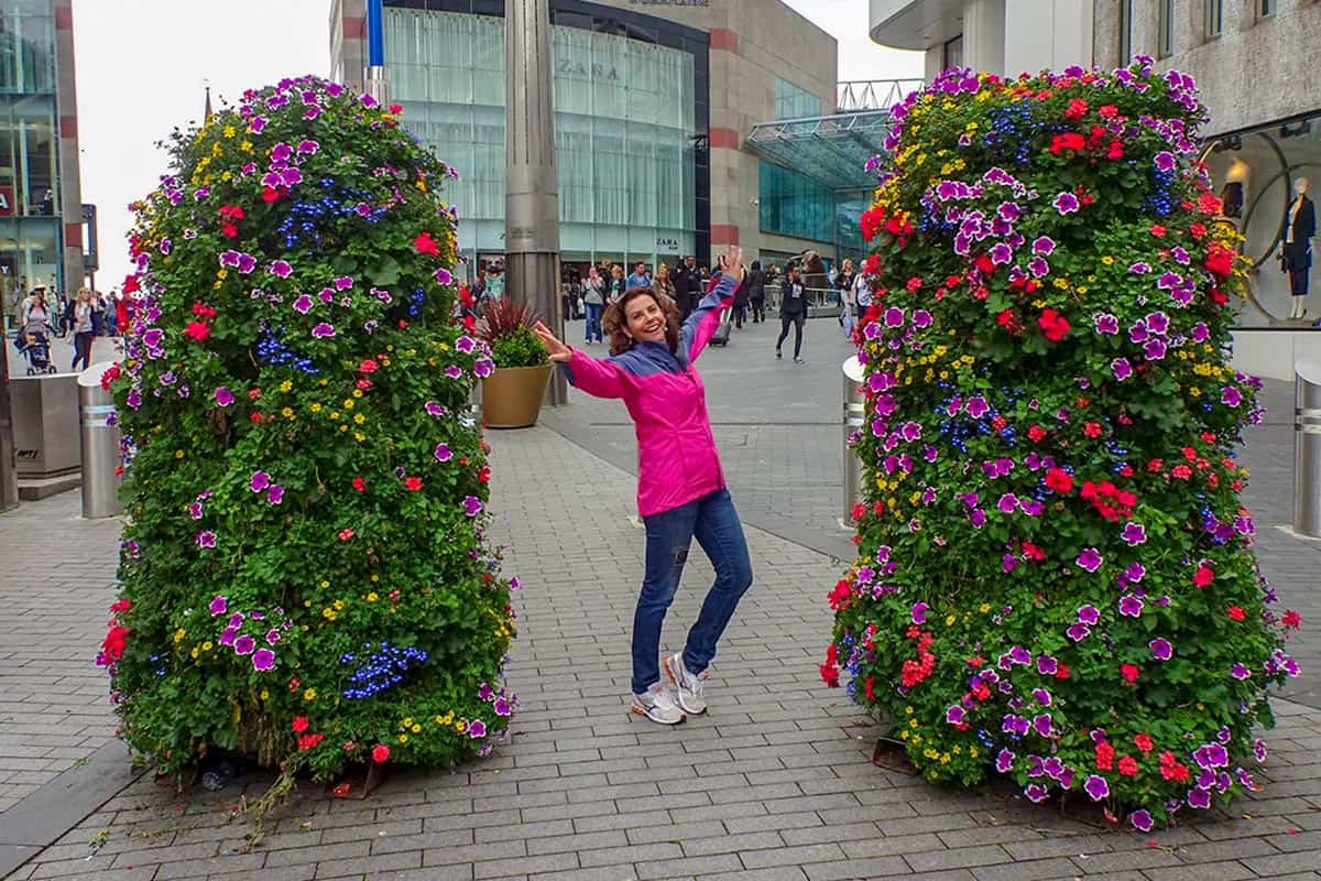 A lady wearing pink jacket dancing between two large flower bushes