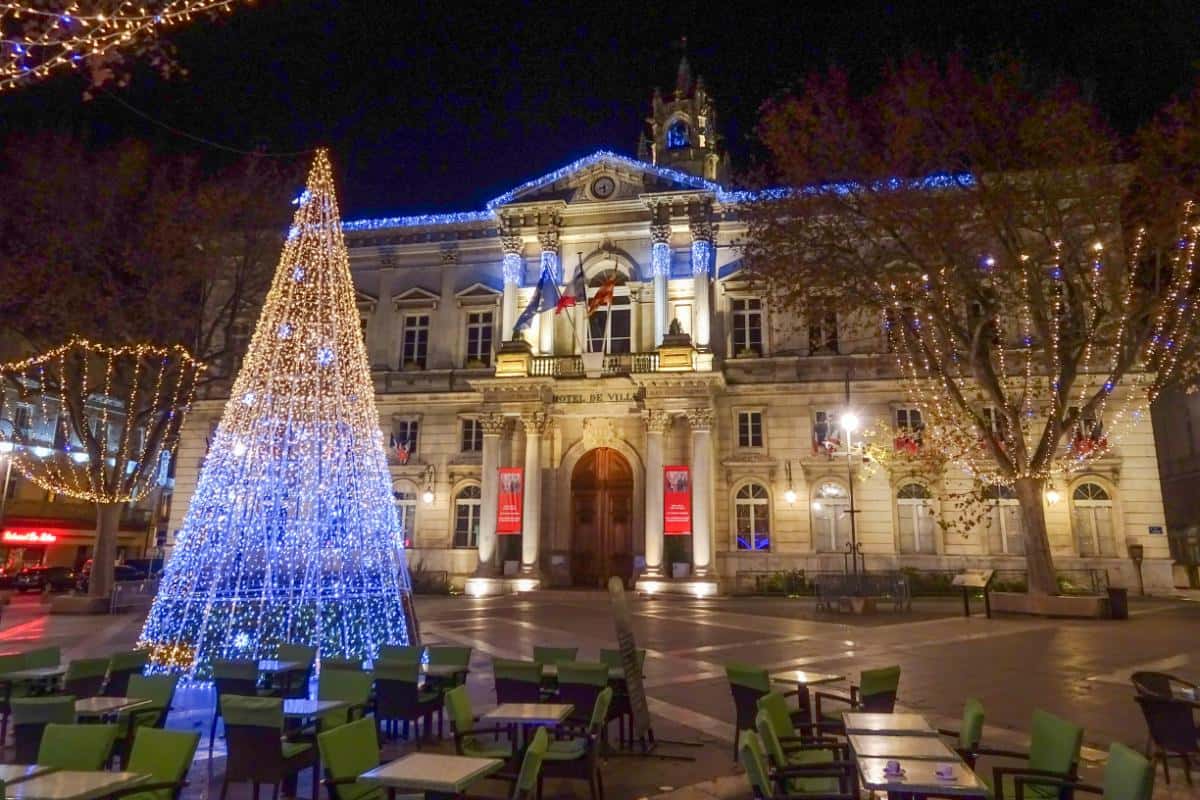 A lit Christmas tree with a town hall in the town square