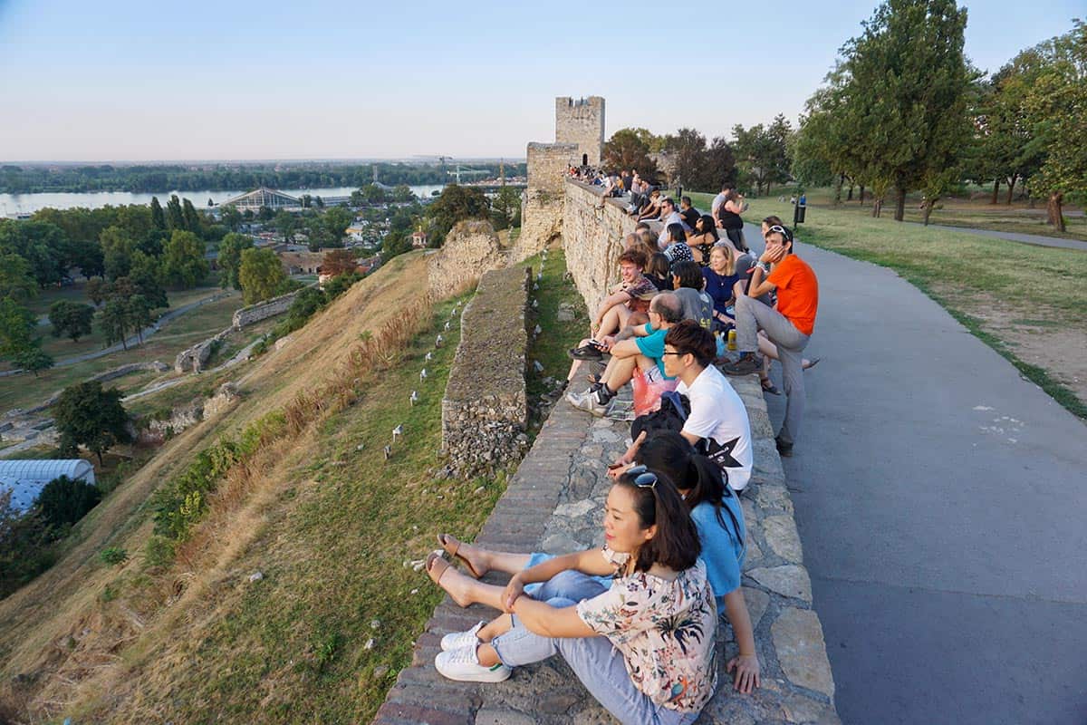 People sitting along a fortress wall looking out to sunset