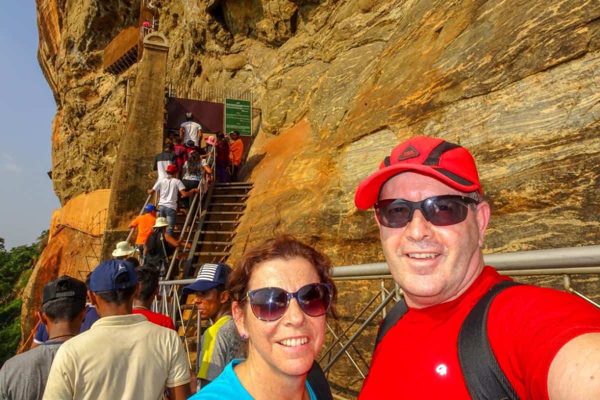 A couple facing the camera with several people in the background climbing a rock staircase